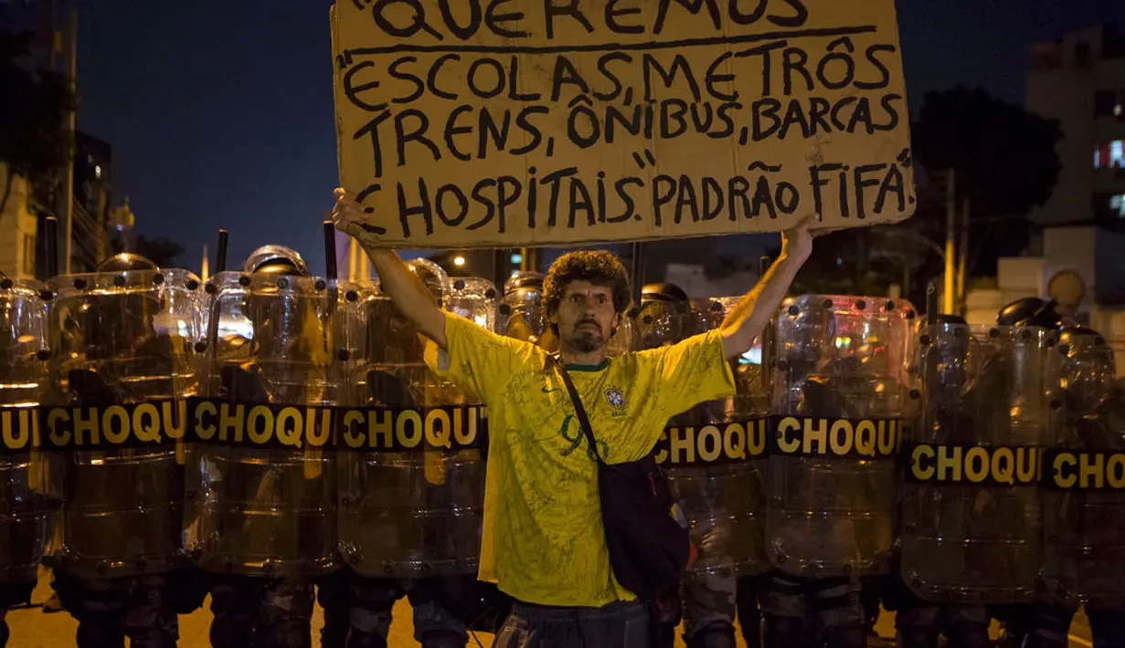 Seorang pengunjuk rasa berdiri di depan polisi anti huru hara selama demonstrasi menentang pengeluaran publik untuk Piala Dunia 2014 di Rio de Janeiro, Brasil, (15/6/2014). (REUTERS/Marco Bello)