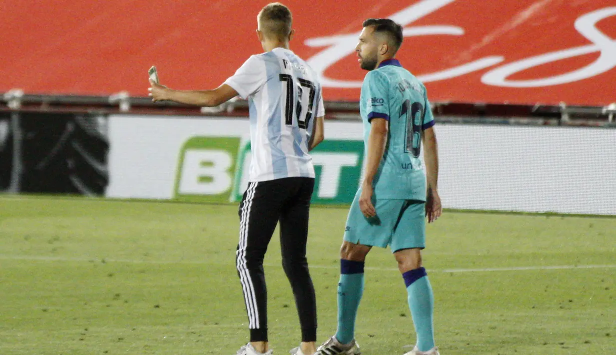 Seorang penyusup (kiri) masuk ke lapangan dan mencoba berswafoto bersama Jordi Alba saat pertandingan La Liga antara Mallorca dengan FC Barcelona di Son Moix Stadium, Palma de Mallorca, Spanyol, Sabtu (13/6/2020). Pertandingan dimenangkan Barcelona dengan skor 4-0. (AP Photo/Francisco Ubilla)