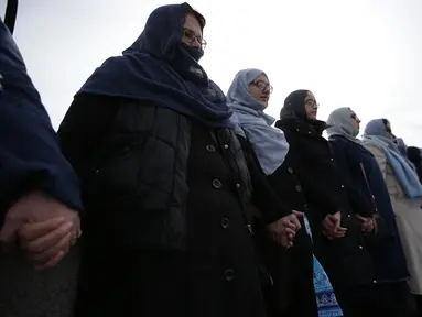 Puluhan perempuan dari beragam etnis bergandengan tangan di Jembatan Westminster, dekat Gedung Parlemen Inggris, London, Minggu (26/3). Mereka mengheningkan cipta selama lima menit untuk mengenang para korban serangan teror London (Daniel LEAL-OLIVAS/AFP)