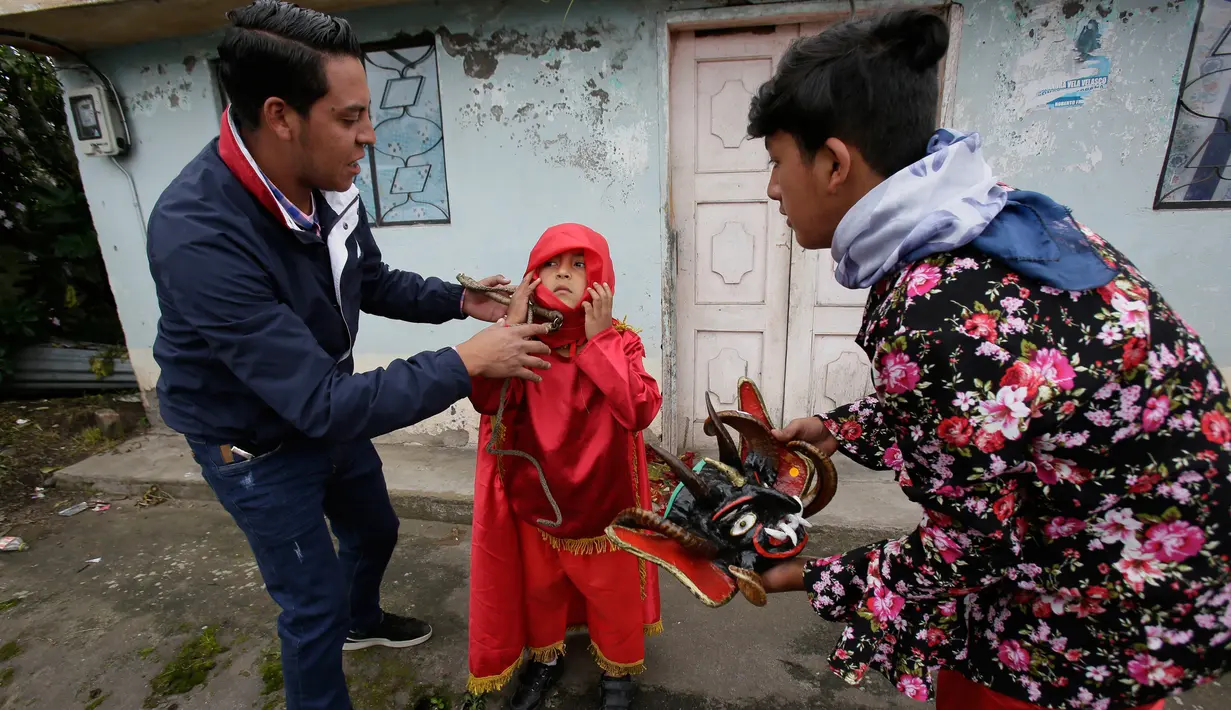 Anak laki-laki dibantu kerabatnya mengenakan kostum selama festival  La Diablada di jalan-jalan kota Pillaro, Ekuador, Jumat (4/1). Festival yang dimulai sejak tahun 1940-an itu untuk merayakan akhir tahun dan memulai tahun baru. (AP/Dolores Ochoa)