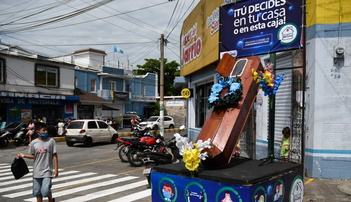 Seorang anak mengamati peti mati dengan tulisan, "Anda memutuskan, di rumah atau di dalam kotak ini", sebagai bagian dari kampanye pemerintah setempat di jalan-jalan kotamadya Escuintla, Guatemala City pada 21 Juli 2020. Kampanye itu upaya untuk menghentikan penyebaran COVID-19. (Johan ORDONEZ/AFP)