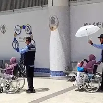 Petugas haji memayungi jemaah haji lansia yang baru tiba di Bandara Prince Mohammed bin Abdulaziz Madinah via jalur fast track. (dok. Dinny Mutiah/MCH 2025)