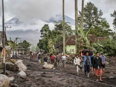 Orang-orang berjalan di tanah yang tertutup abu vulkanik setelah aliran piroklastik selama letusan Gunung Semeru di Desa Supiturang, Lumajang, Jawa Timur pada Kamis 20 November 2025. Gunung Semeru kembali mengalami erupsi pada Rabu (19/11/2025) sore. (Agus Harianto/AFP)