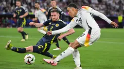 Pemain Jerman, Jamal Musiala (kanan) berusaha melakukan shooting ke gawang Skotlandia dihalangi Anthony Ralston pada laga pembuka Grup A Euro 2024 di Allianz Arena, Munchen, Jerman, Sabtu (15/06/2024) WIB. (AFP/Damien Meyer)