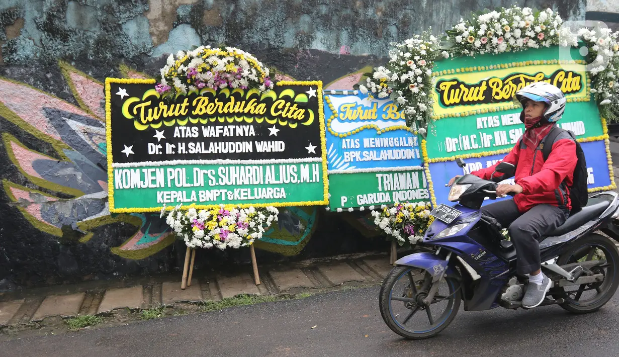 Pengendara melintas dekat karangan bunga duka cita atas meninggalnya KH Salahuddin Wahid atau Gus Sholah di rumah duka Mampang Prapatan, Jakarta, Senin (3/2/2020). Ulama yang juga adik kandung Presiden ke-4 RI Gus Dur itu meninggal dunia pada hari Minggu (2/2/2020). (Liputan6.com/Herman Zakharia)