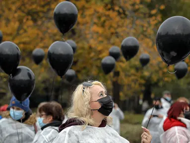 Para petugas medis yang mengenakan masker memegang balon hitam di Bucharest, Rumania, Selasa (17/11/2020). Aksi tersebut untuk mengenang pasien COVID-19 yang tewas dalam kebakaran di instalasi gawat darurat rumah sakit di Piatra Neamt, Rumania pada 14 November 2020 lalu. (AP Photo/Vadim Ghirda)