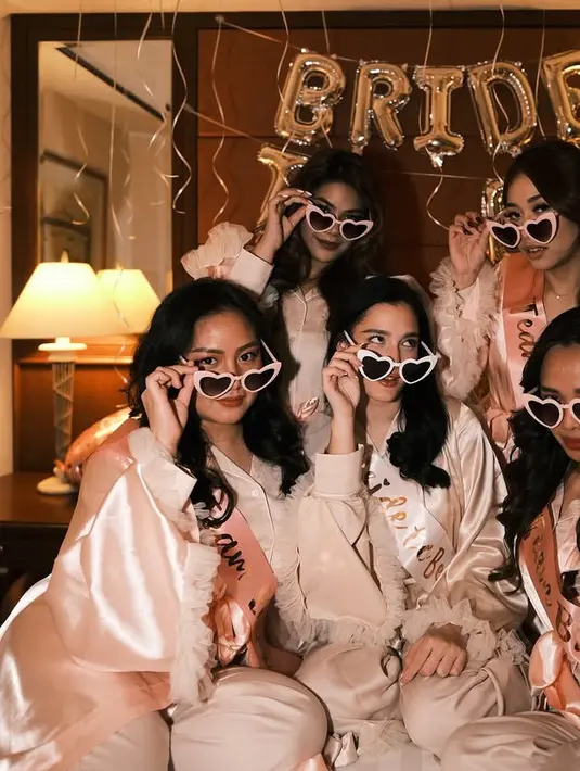 Keempat sahabatnya mengenakan pajamas berwarna soft pink yang memiliki detail renda di bagian lengan. Semakin meraih dengan kacamata frame love putih dan sash bertulisan Team Bride. [@yxsmine.ow]