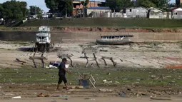 Seorang pria berjalan dan perahu di lahan kering di daerah yang terkena dampak kekeringan dekat Sungai Solimões, Tefe, Amazonas, Brasil, Rabu (19/10/2022). Pemerintah setempat mengatakan terdapat 17 kota dalam status waspada, 39 kota status siaga, dan 3 lainnya dalam keadaan darurat kekeringan. (AP Photo/Edmar Barros)