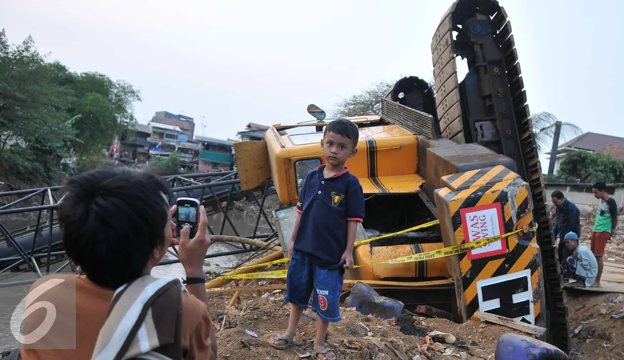 Seorang anak berpose dibelakang crane yang jatuh ke Sungai Ciliwung Kelurahan Bukit Duri, Jakarta Selatan  (1/10/15). Akibatnya seorang warga RT15/10 Kelurahan Bukit Duri, Jakarta Selatan harus mendapatkan perawatan medis. (Liputan6.com/Gempur M Surya)