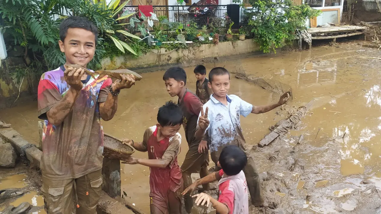 Dengan rona wajah ceria, Firdasu dan rekannya, nampak asik dan ceria ‘ngubek balong’ atau mencari ikan yang tersisa di kolam milik warga setelah musibah banjir bandang menyapu kampungnya.