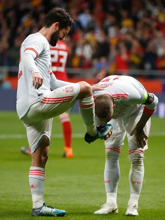 Ekspresi pemain Spanyol, Isco Alarcon saat sepatunya dicium oleh Sergio Ramos usai ia mencetak gol saat pertandingan persahabatan melawan Argentina di stadion Wanda Metropolitano di Madrid (27/3). Isco berhasil mencetak tiga gol. (AP Photo / Paul White)