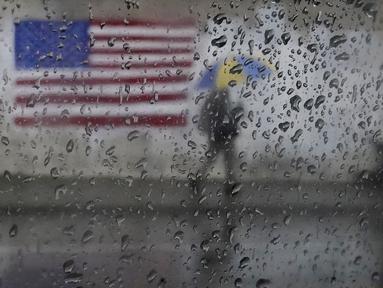 Seorang pejalan kaki membawa payung sambil berjalan melewati lukisan bendera Amerika di San Francisco, Rabu (11/1/2023). California yang dilanda badai berjuang untuk membersihkan dan memperbaiki kerusakan yang meluas. (AP Photo/Jeff Chiu)
