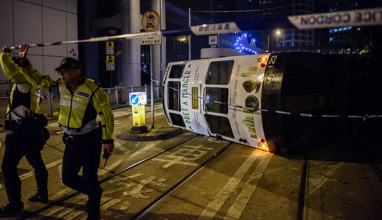 Petugas kepolisian memblokir lokasi sebuah trem double-decker yang terbalik di jalan utama di Hong Kong, Kamis (6/4). Hong Kong telah mengoperasikan tram, yang dikenal sebagai 'ding-ding' lebih dari satu abad lalu. (ANTHONY WALLACE/AFP)