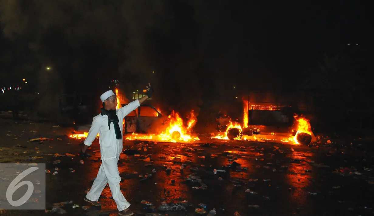 Seorang pendemo melintas di dekat mobil yang terbakar di kawasan Monas, Jakarta, Jumat (4/11). Aksi Damai 4 November ini berakhir ricuh dengan terjadi bentrok antara pendemo versus polisi. (Liputan6.com/Angga Yuniar)