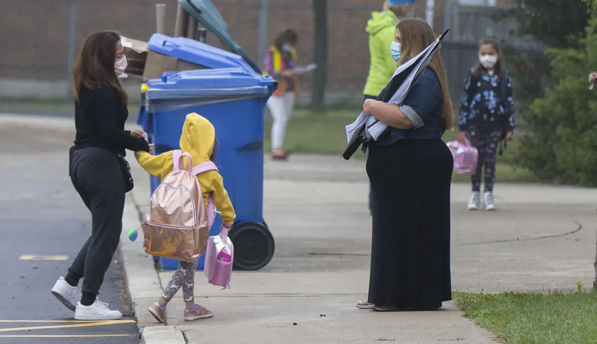 Seorang guru yang memakai masker (kanan) menyapa murid di luar sekolah di Mississauga, Ontario, Kanada  (9/9/2020). Beberapa sekolah di Ontario dibuka kembali pada Rabu (9/9), menawarkan kombinasi kelas tatap muka dan pembelajaran daring (online) bagi para murid. (Xinhua/Zou Zheng)