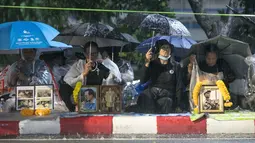Pelayat menggunakan payung sambil menunggu hujan demi menghadiri upacara kremasi Raja Thailand Bhumibol Adulyadej di Bangkok, Selasa (24/10). Prosesi kremasi Raja Bhumibol dilaporkan telah menelan biaya hingga sekitar Rp1,2 triliun. (AP/Wason Wanichakorn)