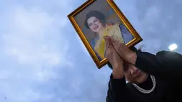 Seorang pelayat memegang potret Ratu Sirikit setelah iring-iringan mobil di Bangkok, Thailand pada Minggu 26 Oktober 2025. Persemayaman Ratu Sirikit berlangsung selama setahun dimulai pada 26 Oktober 2025 di Grand Palace, Bangkok, Thailand, setelah beliau meninggal dunia pada 24 Oktober 2025. (Chanakarn Laosarakham/AFP)