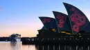 Kapal pesiar menuju Sydney Harbour saat layar Opera House diterangi oleh proyeksi bunga poppy selama Remembrance Day Dawn Service di Sydney, Jumat (11/11/2022). Bunga poppy merah menjadi simbol untuk mengenang mereka yang meninggal selama perang. (Saeed KHAN / AFP)
