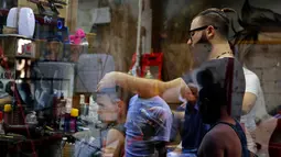 Muhannad Khaled Omar memotong rambut pelanggannya di Burj al-Barajneh, Lebanon (14/7). (AP Photo / Bilal Hussein)