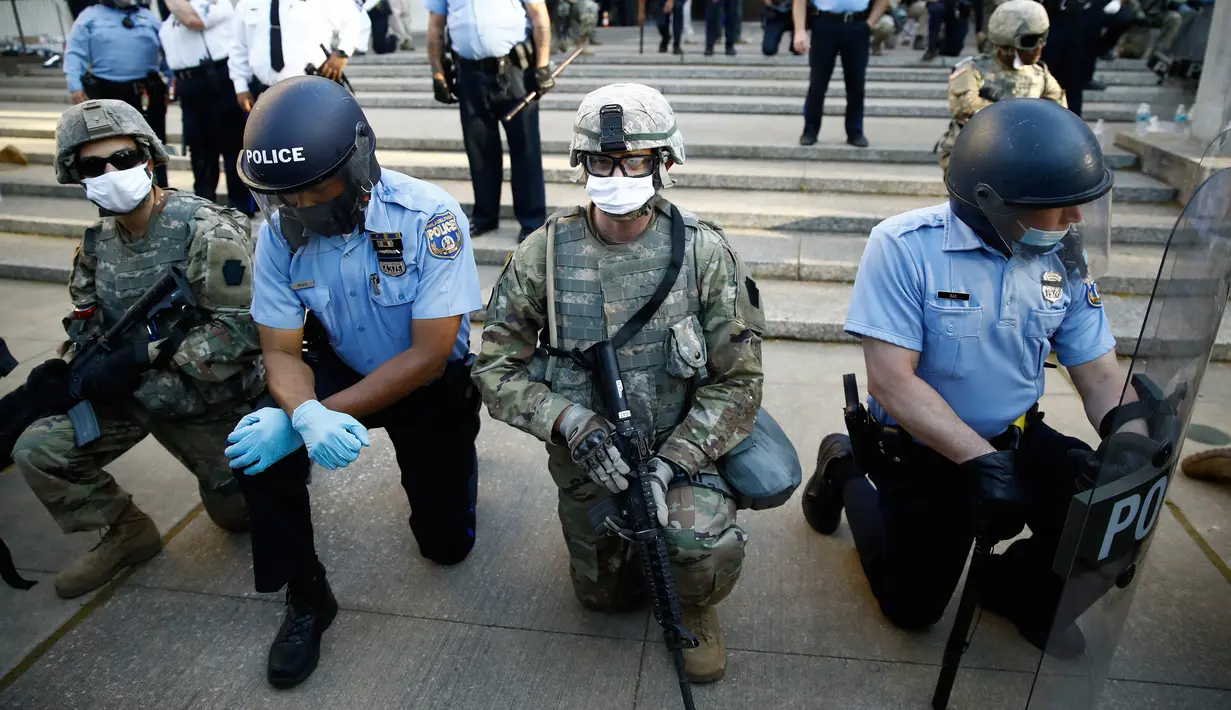 Polisi dan Garda Nasional Philadelphia berlutut saat pawai menyerukan keadilan atas kematian George Floyd di luar markas besar Kepolisian Philadelphia, Senin (1/6/2020). George Floyd tewas tak bisa bernafas karena tercekik lutut polisi saat ditangkap pada (25/5/2020) lalu. (AP/Matt Rourke)