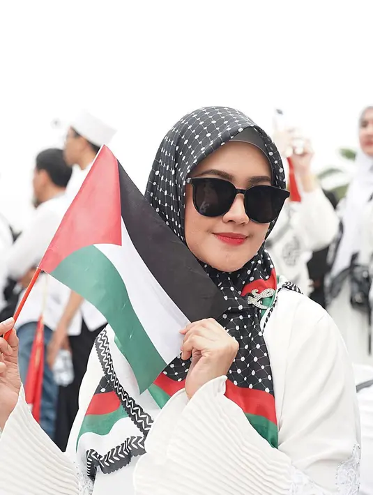 Tidak bersama Tommy Kurniawan, Lisya Nurrahmi hadir dalam aksi bela Palestina bersama rekan selebriti lainnya. Lisya tampil dengan gamis putih, pakai jilbab dengan motif bendera Palestina, dan tak lupa memakai kacamata untuk menghindari silau cahaya matahari. Selain membawa bendera Palestina, Lisya juga mencoret pipi sebelah kanan dengan gambar bendera Palestina. (Liputan6.com/IG/@lisyanurrahmii)