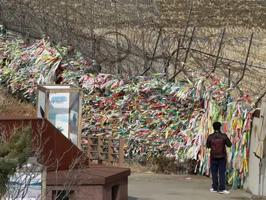 Seorang pria berjalan di dekat pagar kawat yang dihiasi ribuan pita bertuliskan pesan damai antara Korea Selatan dan Korea Utara di Paviliun Imjingak, Paju, Korea Selatan, Senin (5/3). (AP Photo/Lee Jin-man)