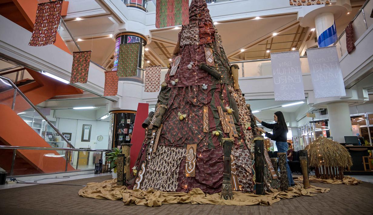 Mengangkat tema Terang dari Timur, dekorasi Pohon Natal pada tahun ini dihadirkan dengan nuansa Papua dan dapat dinikmati pengunjung hingga 31 Januari 2026 di ruang pameran Perpustakaan lantai 6 kampus PCU. Tampak dalam foto, salah satu mahasiswa memasang sentuhan akhir pada instalasi dekorasi berbentuk pohon Natal dengan motif budaya Papua di Perpustakaan Petra Christian University (PCU), Surabaya, Jawa Timur, Kamis 18 Desember 2025. (JUNI KRISWANTO/AFP)