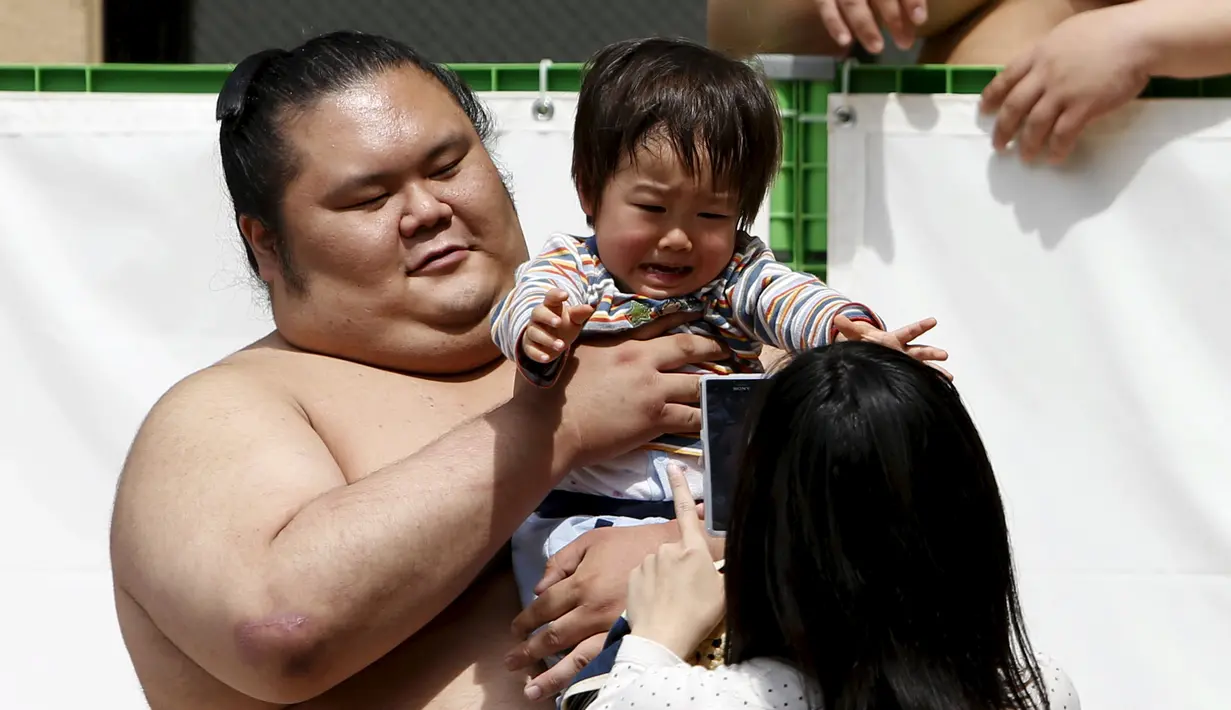 Seorang pesumo menggendong bayi sebelum dimulainya kejuaraan sumo, Honozumo, di Kuil Yasukuni, Tokyo, Senin (18/4). Selain menjadi ajang kejuaraan olahraga tradisional jepang, kejuaraan tahunan itu juga menjadi daya tarik wisata. (REUTERS/Yuya Shino)