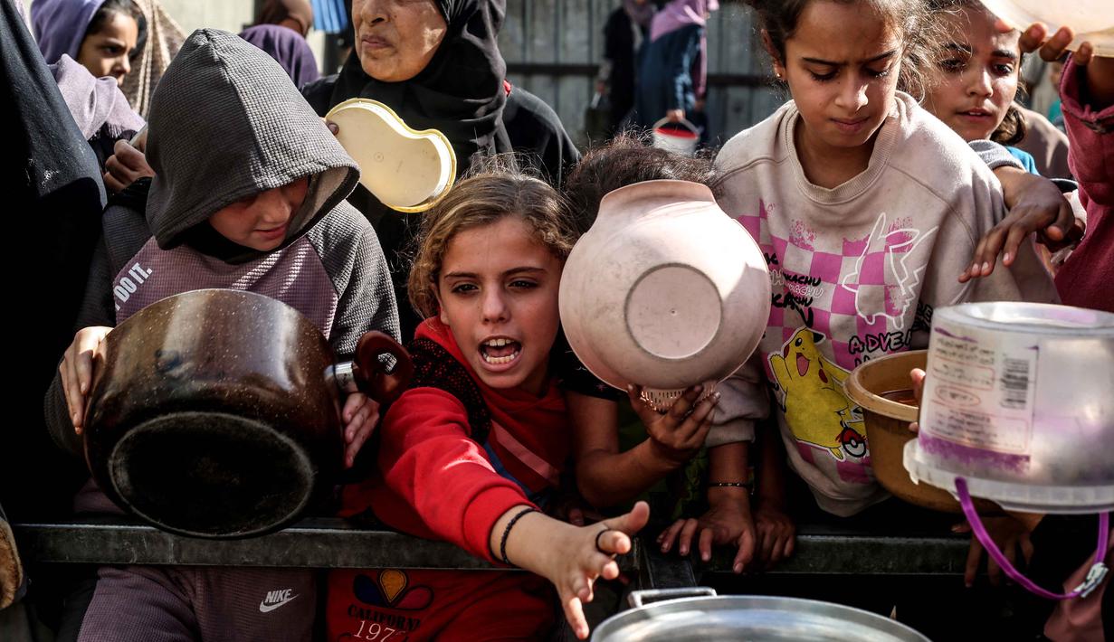 Sebelumnya, badan-badan kemanusiaan meyakini bahwa begitu hambatan administrasi dan akses logistik dihapus, mereka sebenarnya memiliki cukup material untuk menopang hampir 1,5 juta warga Palestina yang sangat membutuhkan bantuan. Tampak dalam foto, anak-anak Palestina yang terlantar menunggu makanan di sebuah tempat penampungan tempat tinggal keluarga-keluarga di Nuseirat, pusat Jalur Gaza, pada 23 November 2025. (EYAD BABA/AFP)