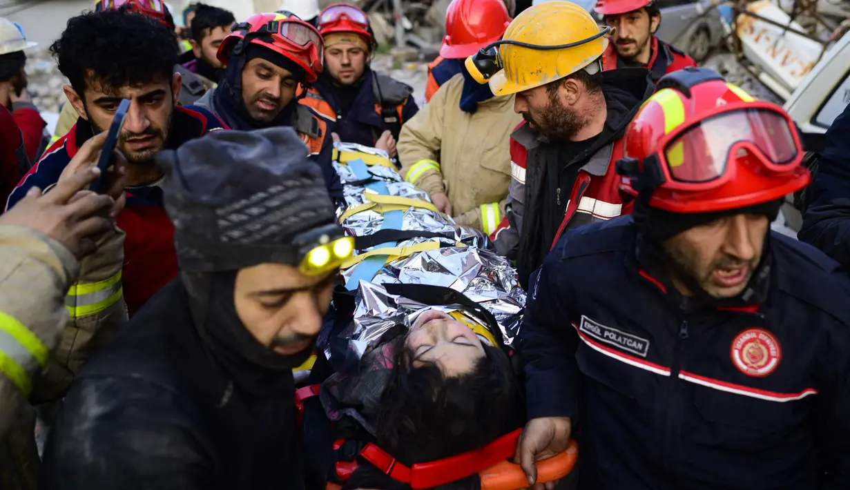 Tim penyelamat mengevakuasi seorang gadis Suriah berusia 12 tahun, Cudi, dari puing-puing bangunan yang hancur di Hatay, Turki, setelah gempa berkekuatan 7,8 melanda tenggara negara itu, Minggu (12/2/2023). Tim penolong mulai kelelahan mencari korban selamat di puing-puing akinbat gempa Turki dan Suriah, ketika korban tewas sudah mencapai 28.000 dan tampaknya akan terus bertambah. (Photo by Yasin AKGUL / AFP)