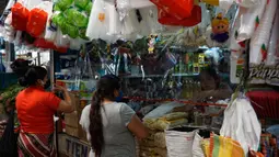 Pelanggan berbelanja dengan sekat tirai pelindung plastik pada kios jualan di pasar La Asuncion di Villa Nueva, Guatemala City pada 20 Juli 2020. Kios di pasar itu menggunakan tirai pelindung plastik untuk menjaga jarak fisik guna mengurangi resiko penyebaran virus Corona. (Johan ORDONEZ/AFP)