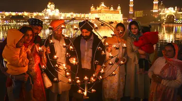 Umat Sikh menyalakan lampu tanah di Kuil Emas yang diterangi pada peringatan kelahiran Guru Nanak di Amritsar, India, 19 November 2021. Guru Nanak adalah Guru Sikh pertama dan pendiri Sikhisme. (AP Photo/Prabhjot Gill)