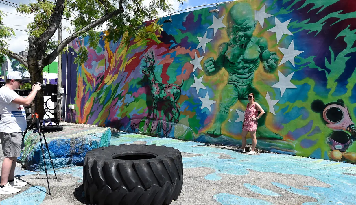 Pengunjung berpose di depan mural karya seniman Ron English di kawasan Wynwood, Miami, Florida pada 28 September 2016. Goldman Properties menggelar pameran mural untuk merevitalisasi lingkungan. (AFP PHOTO / Rhona WISE)