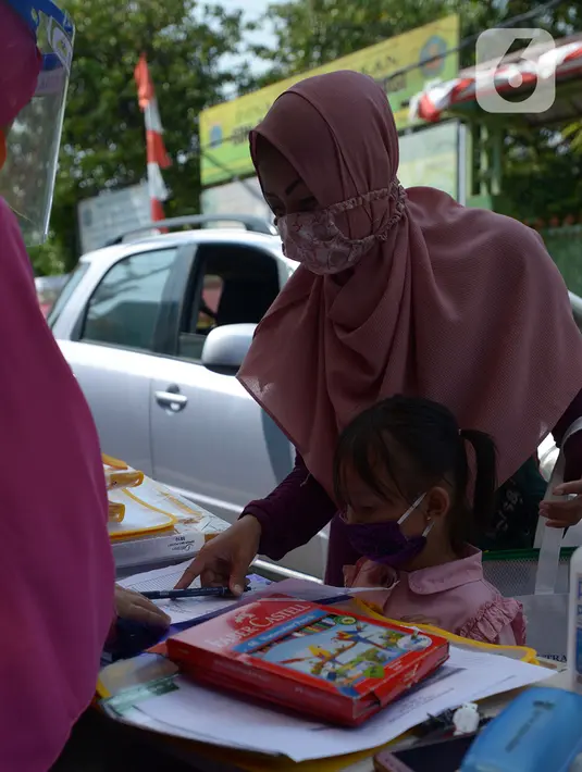 Wali murid mengambil tugas sekolah secara drive-thru dari guru SDIT Ibnu Sina di Jakarta, Rabu (26/8/2020). Selama pembelajaran jarak jauh, siswa diwajibkan mengambil dan mengembalikan tugas di sekolah. (merdeka.com/Imam Buhori)