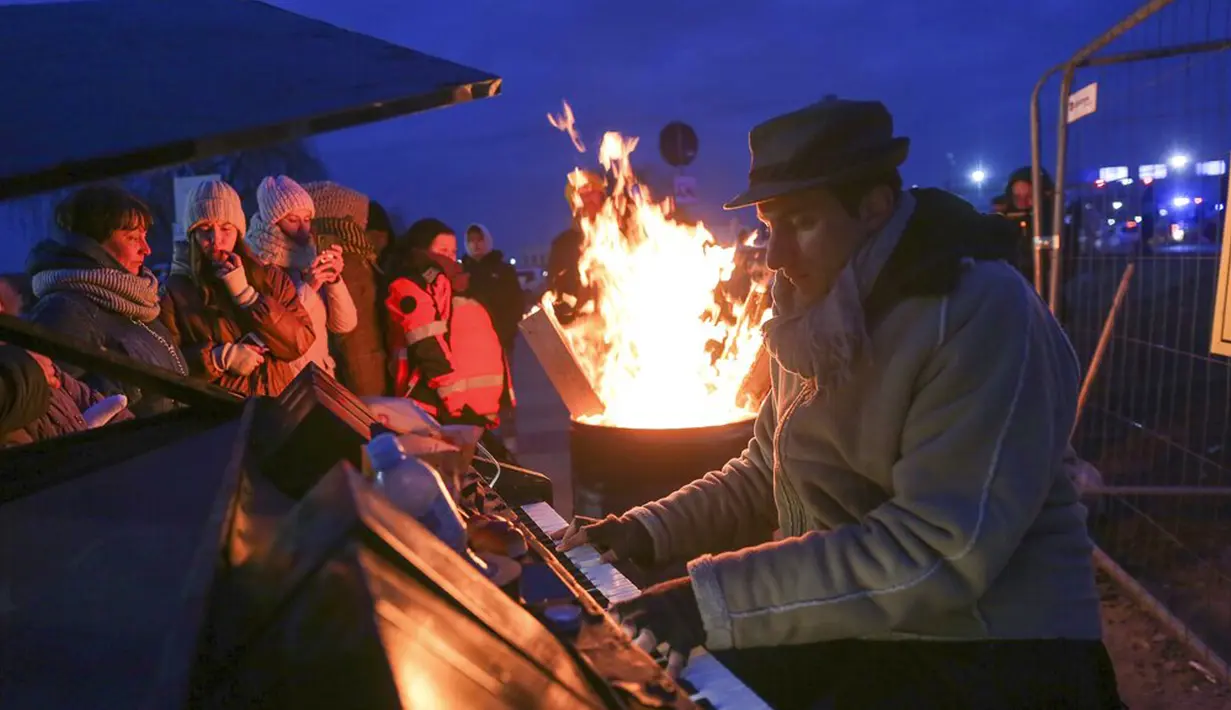 Orang-orang berkumpul di sekitar pianis Italia Davide Mortarelli yang tampil untuk para pengungsi yang melarikan diri dari perang Ukraina di perbatasan yang melintasi Medyka, Polandia, 4 Maret 2022. (AP Photo/Visar Kryeziu)