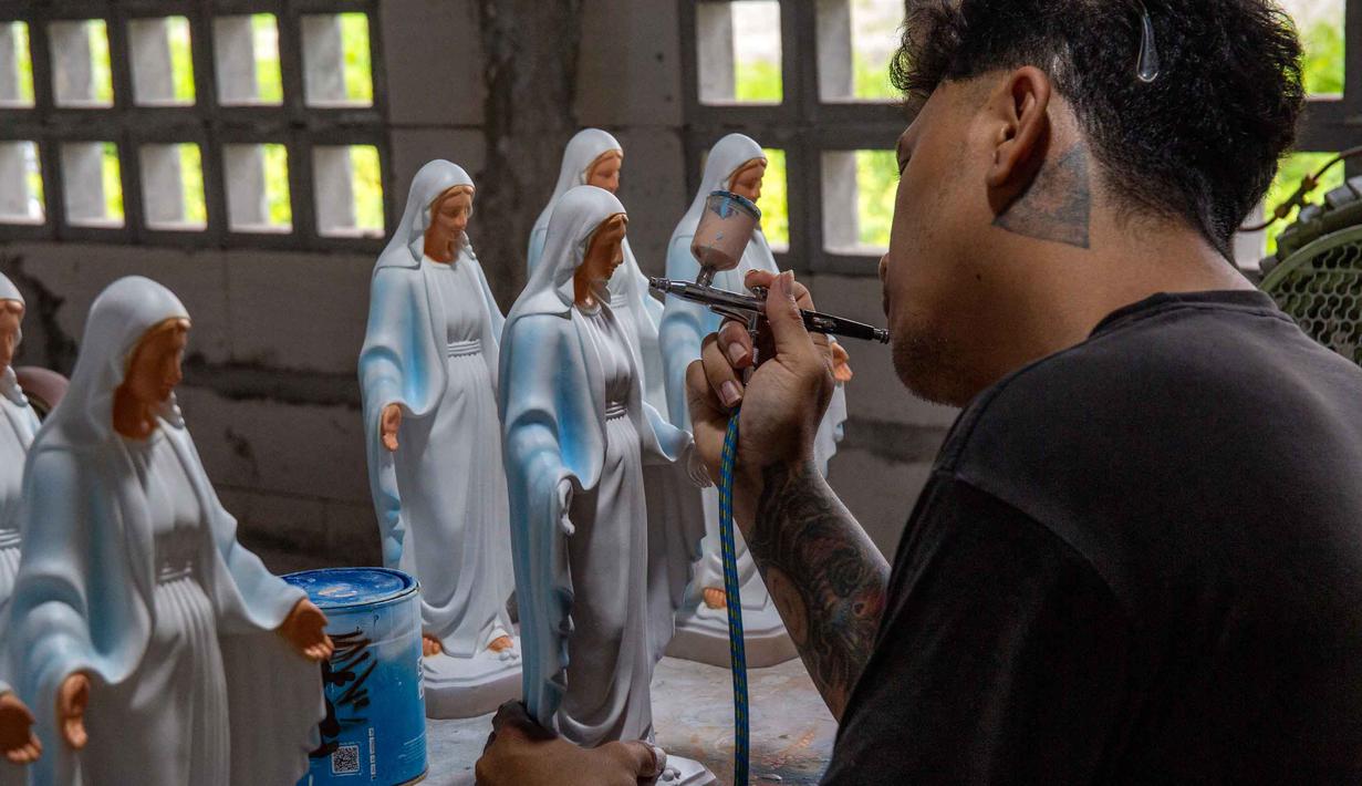 Peningkatan pesanan terjadi sejak beberapa bulan lalu. Tampak dalam foto, seorang pekerja menyemprotkan cat ke patung-patung keagamaan Kristen di bengkel kerajinan Studio Malta Jaya di Bantul, Yogyakarta, pada Kamis 18 Desember 2025. (DEVI RAHMAN/AFP)