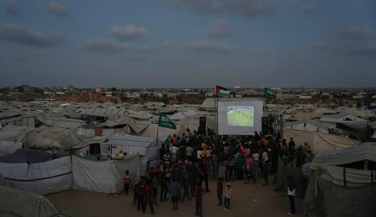 Warga Palestina menyaksikan siaran langsung pertandingan sepak bola Piala Dunia antara Spanyol dan Arab Saudi melalui layer lebar di Nuseirat, Jalur Gaza Tengah, Minggu 21 Juni 2026. (AP Photo/Abdel Kareem Hana)