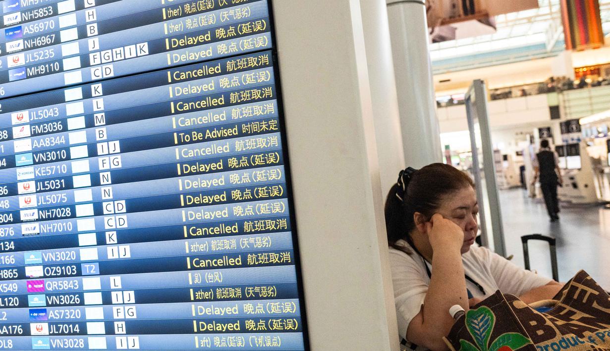 Seorang wanita beristirahat di samping papan informasi penerbangan di Terminal Internasional Bandara Haneda setelah penerbangan dibatalkan atau ditunda karena badai tropis Jangmi di Tokyo, Jepang, Rabu 3 Juni 2026. (Andrew CAALLERO-REYNOLDS/AFP)