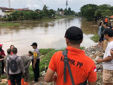 Warga bersama personel kepolisian, Satpol PP, dan TNI berkumpul di bantaran Sungai Ciliwung, Jakarta, Selasa (25/2/2020). Adanya warga yang hanyut saat berenang di tengah luapan Sungai Ciliwung mengundang perhatian warga dan petugas yang mencari keberadannya. (Liputan6.com/Immanuel Antonius)
