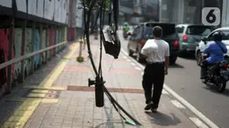 Pejalan kaki melintasi samping instalasi kabel yang semrawut di Jalan Kyai Maja, Kebayoran Baru, Jakarta Selatan, Rabu (11/11/2020). Kurangnya penataan menjadi penyebab instalasi kabel di Ibu Kota kian semrawut sehingga mengganggu kenyamanan serta keselamatan warga. (Liputan6.com/Immanuel Antonius)