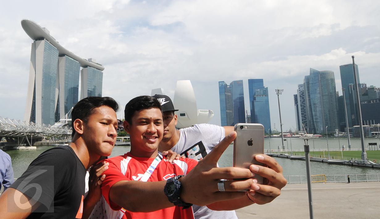 Para penggawa Garuda Muda bersantai sejenak usai melaksanakan ibadah salat Jumat di Masjid Sultan, Bugis, Singapura (5/6). Yandi Sofyan, M Natshir dan Agung Prasetyo (kiri-kanan) ber-selfie berlatar Marina Bay Sand. (Liputan6.com/Helmi Fithriansyah)