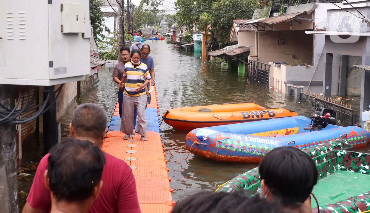 Warga berjalan melintasi jembatan apung saat banjir melanda Perumahan Periuk Damai, Tangerang, Banten, Selasa (23/2/2021). Adanya jembatan apung mempermudah warga saat melintasi banjir setinggi 2,5 meter di tempat tersebut. (Liputan6.com/Angga Yuniar)