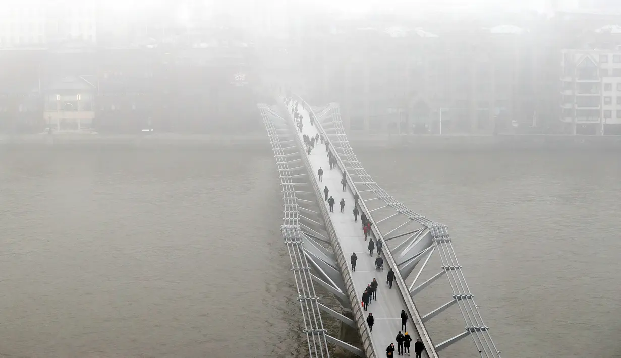 Pejalan kaki berjalan di atas jembatan Millennium Katedral di London, Senin, (23/1). Ribuan penumpang pesawat di Bandara Heathrow terpaksa ditunda keberangkatannya karena cuaca buruk ini. (AP Photo / Kirsty Wigglesworth)
