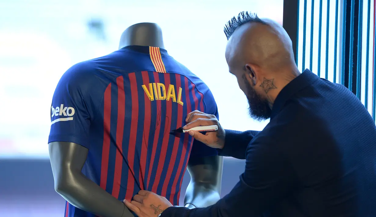 Pemain baru Barcelona, Arturo Vidal menandatangani jersey dalam presentasi resminya di Stadion Camp Nou, Barcelona, Spanyol, Senin (6/8). (Josep LAGO/AFP)