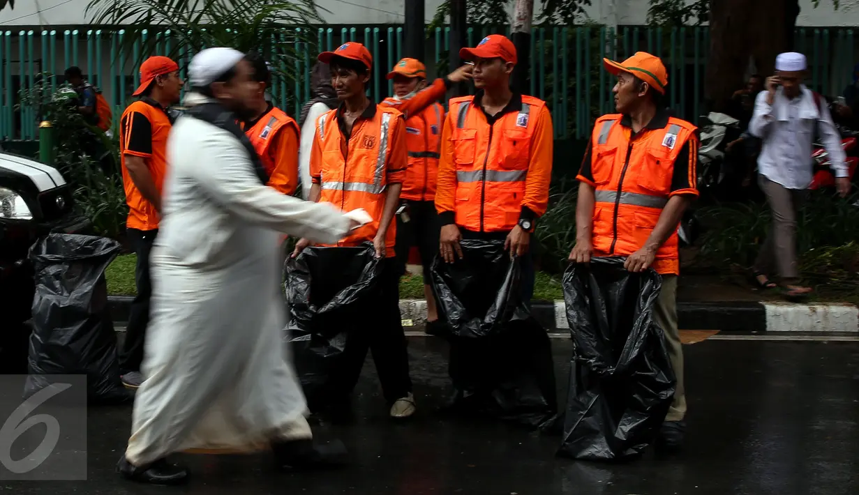 Seorang pejalan kaki melewati sejumlah pasukan oranye (petugas kebersihan) yang disiagakan di kawasan Monas, Jakarta, Jumat (2/12). Pasukan oranye disiagakan untuk menjaga kebersihan lingkungan saat aksi damai 2 Desember. (Liputan6.com/Johan Tallo)