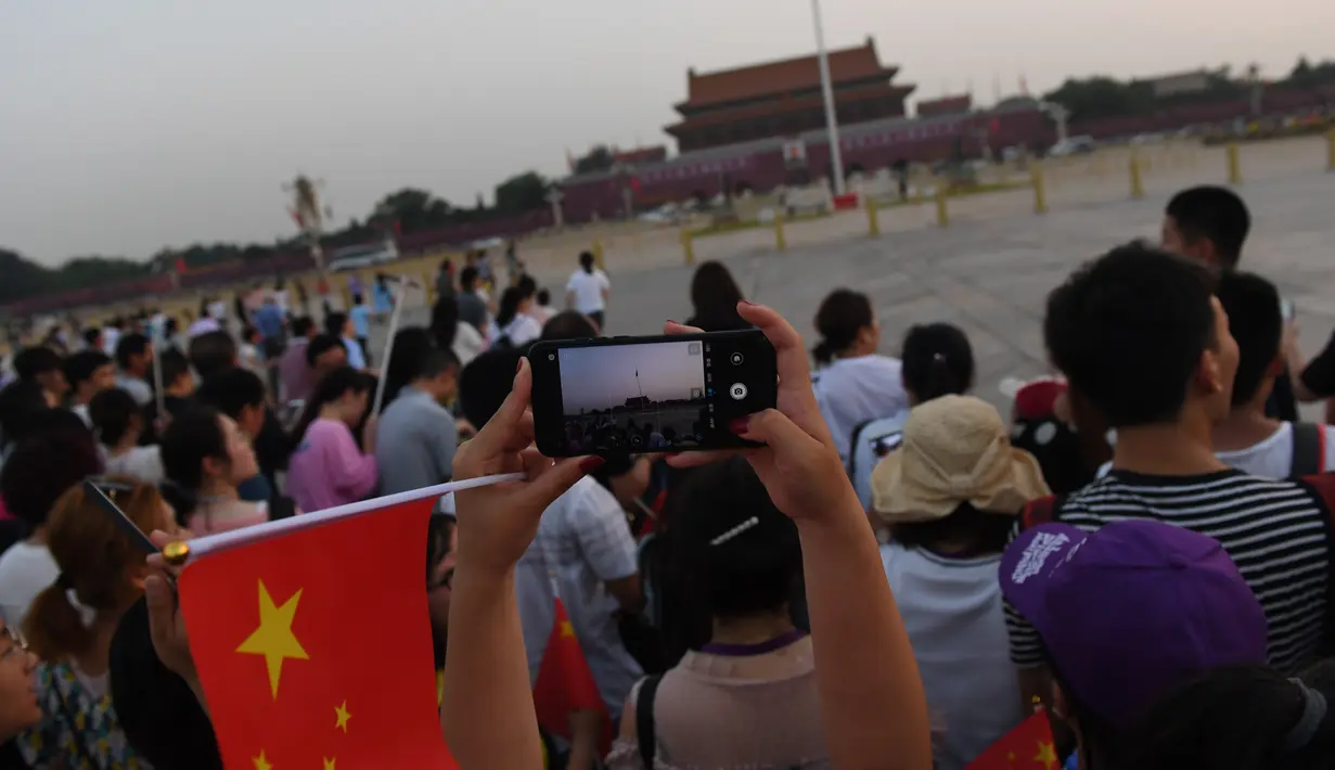 Warga mengambil foto setelah upacara pengibaran bendera saat fajar setelah kematian mantan perdana menteri China Li Peng di Lapangan Tiananmen Beijing (24/7/2019). Li Peng meninggal dunia akibat menderita kanker kandung kemih. (AFP Photo/Greg Baker)