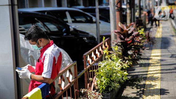 Seorang pegawai bermain ponsel sambil berjemur di bawah sinar matahari di Kawasan Fatmawati, Jakarta, Selasa (31/3/2020). Berjemur diri di bawah sinar matahari saat pagi merupakan salah satu upaya yang paling sederhana untuk menjaga kesehatan selama wabah virus COVID-19. (Liputan6.com/Faizal Fanani)