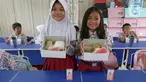 Dua siswi Sekolah Dasar (SD) Angkasa 5 Halim Perdanakusuma memperlihatkan makanan yang tersaji di dalam kotak saat uji coba program makan bergizi gratis, Jakarta, Selasa (26/11/2024). (Liputan6.com/Herman Zakharia)