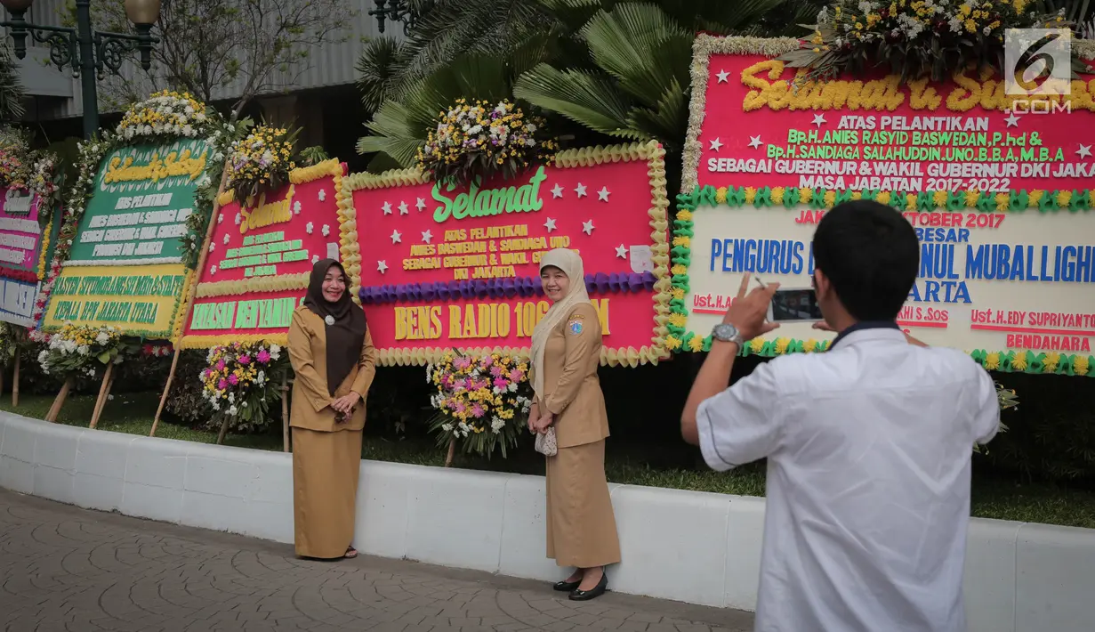 Pegawai Pemprov DKI berfoto di depan karangan bunga ucapan selamat atas pelantikan Gubernur dan Wakil Gubernur DKI terpilih, Anies Baswedan dan Sandiaga Uno di Halaman Balai Kota DKI Jakarta, Senin (16/10). (Liputan6.com/Faizal Fanani)