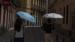 Dua perempuan berjalan dengan payung di pusat kota Madrid, Spanyol, Minggu (12/6/2022). Layanan cuaca Spanyol mengatakan massa udara panas dari Afrika utara memicu gelombang panas besar pertama di negara itu tahun ini dengan suhu diperkirakan naik hingga 43 derajat Celcius (109 derajat Fahrenheit) di area tertentu. (AP Photo/Paul White)